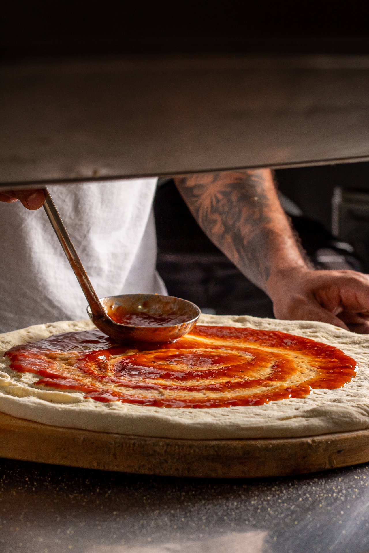 Pizzaiolo espalhando molho de tomate na massa